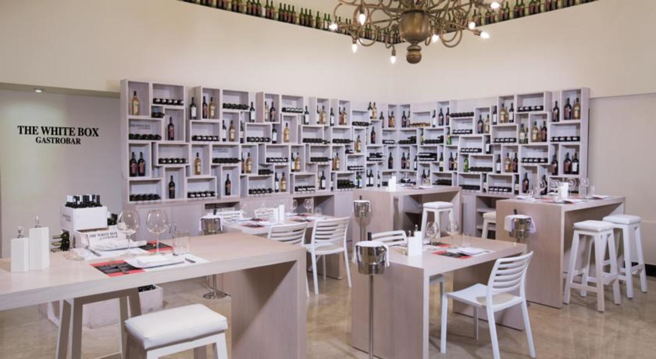 Grand Oasis Palm Hotel Cancún Exterior foto The photo shows a modern restaurant interior. The walls are lined with shelves that display a variety of bottles, likely wine or spirits, creating a visually striking backdrop. The dining area features wooden tables and white chairs, offering a clean