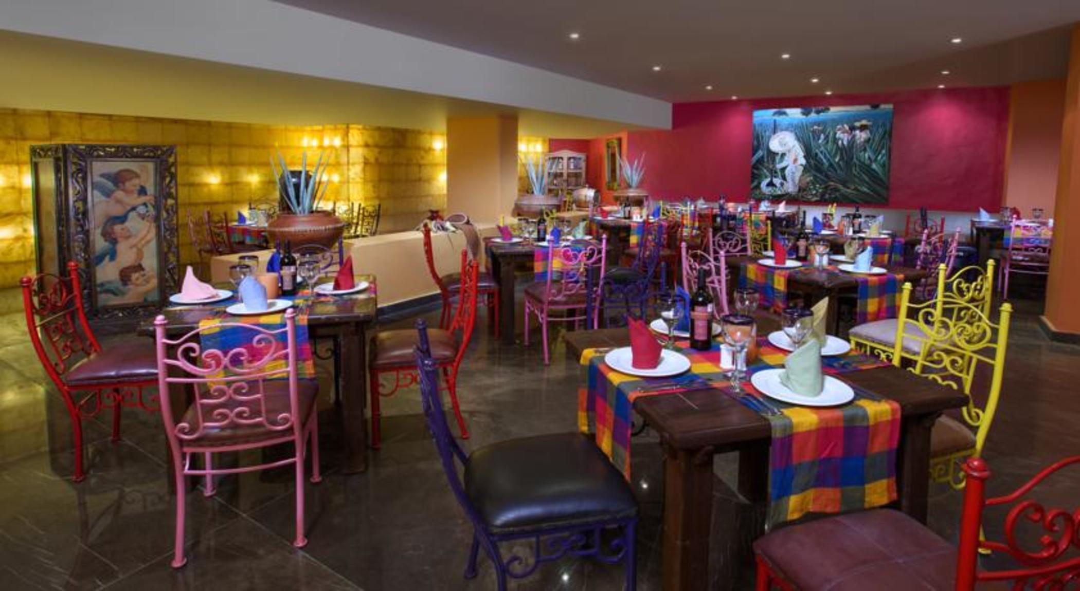 Grand Oasis Palm Hotel Cancún Exterior foto The photo shows a vibrant and colorful restaurant interior. There are several tables arranged with multicolored tablecloths, each adorned with plates and decorative napkins. The chairs are also colorful, featuring a mix of pink, purple, and metal des