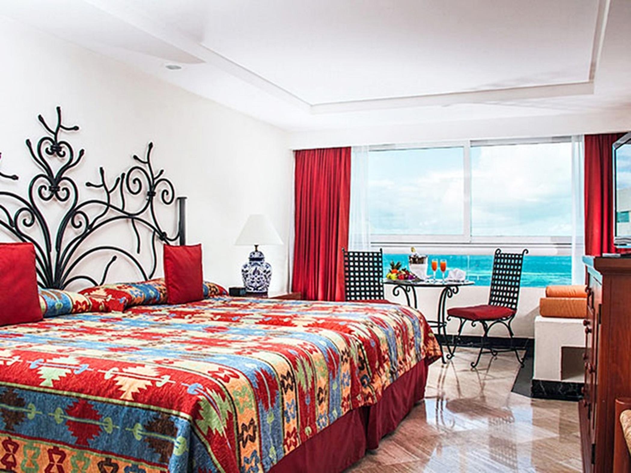 Grand Oasis Palm Hotel Cancún Exterior foto The photo shows a well-decorated hotel room featuring two large beds with vibrant, patterned bedding. The headboards are stylishly designed, and the room has colorful accents like red curtains and cushions. A small table with chairs is positioned by 