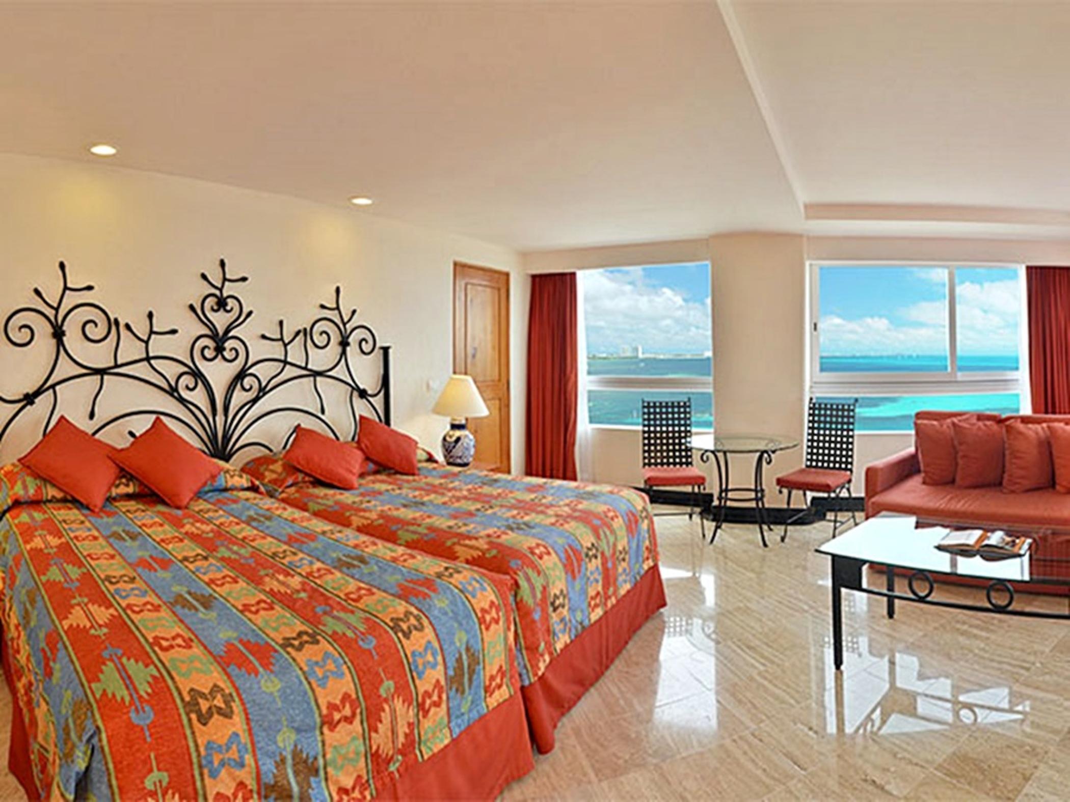 Grand Oasis Palm Hotel Cancún Exterior foto The photo shows a spacious hotel room featuring two beds with colorful patterned bedding. The walls are decorated with a decorative iron headboard. There are large windows that provide a view of the ocean and a bright, sunny sky. The room is warmly l