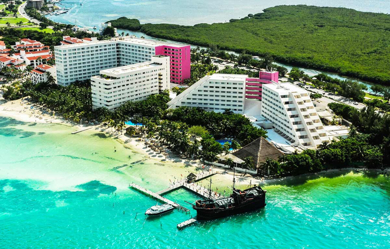 Grand Oasis Palm Hotel Cancún Exterior foto The photo shows an aerial view of a resort area located near a beach. There are several large buildings, with a mix of white and pink architecture. The buildings are surrounded by lush greenery and palm trees, creating a tropical atmosphere. 

In the